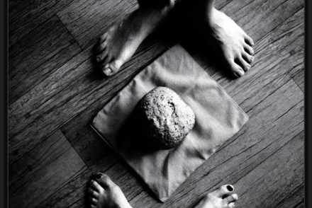 a loaf of bread on the floor, two pairs of feet on either sides of it